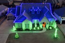 Two-story stone home glowing with blue roofline and green tree lighting